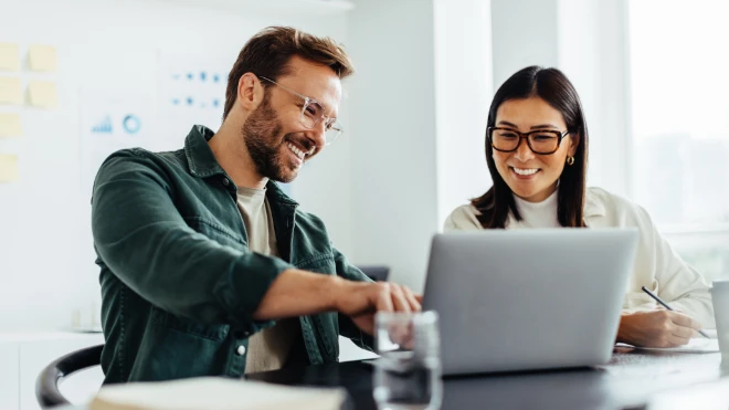 two coworkers discussing something on a laptop