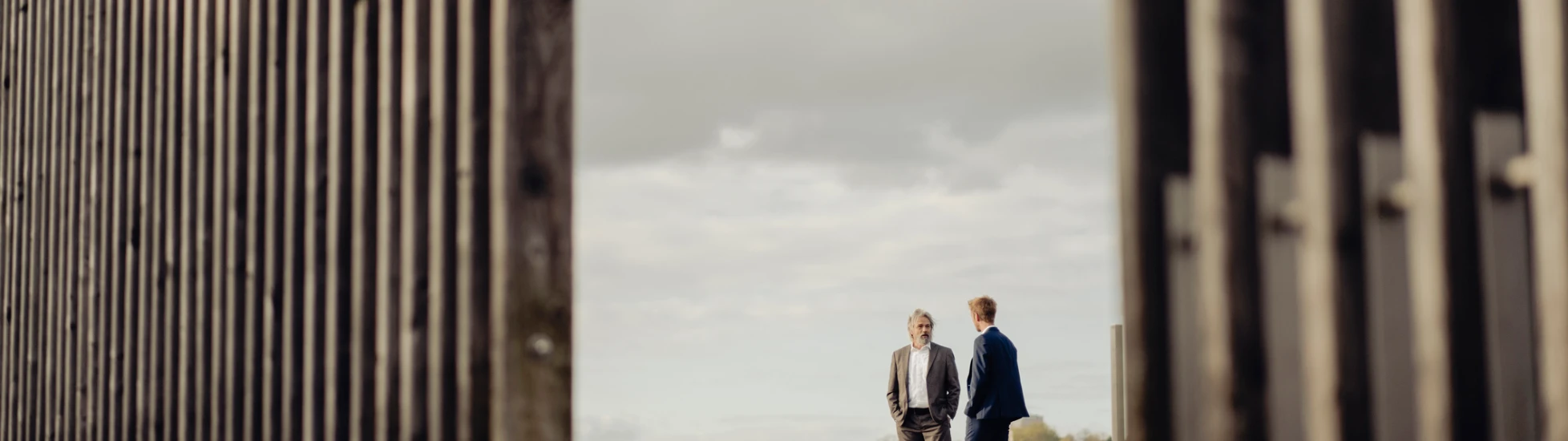 Two businessmen standing behind fencing